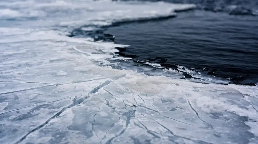 The edge of sea ice where the solid surface meets dark open water, with fracture lines visible